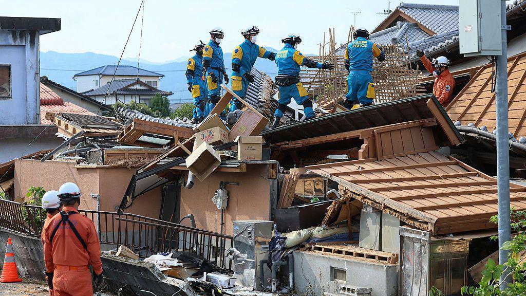 Rescue workers in overalls stand on top of a collapsed house