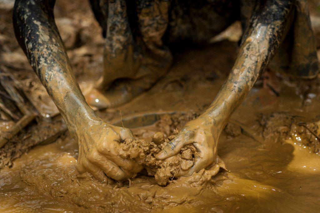 A gold panner picks up clumps of muddy sediment with his hands in Kibi on 10 April 2017