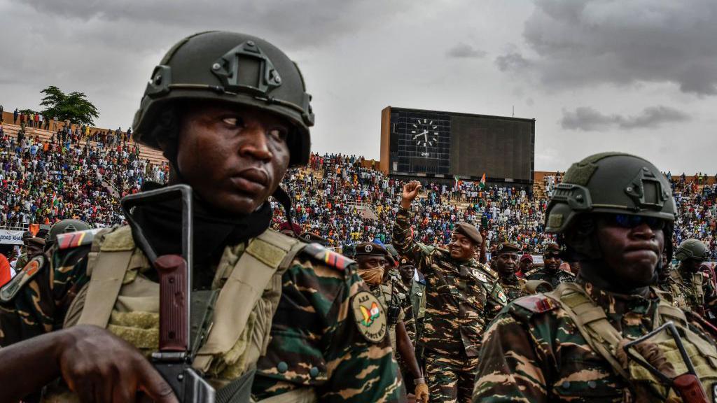 Flanked by troops, Niger's coup leader Gen Abdourahamane Tchiani (C) greets the thousands of people at a  stadium in Niamey on 26 July 2023. They are all wearing camouflage.