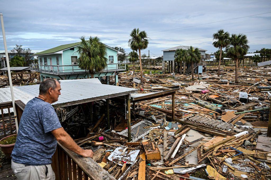 A man inspects the damage of his home after Hurricane Helene. The image shows debris from houses as far as the eye can see.