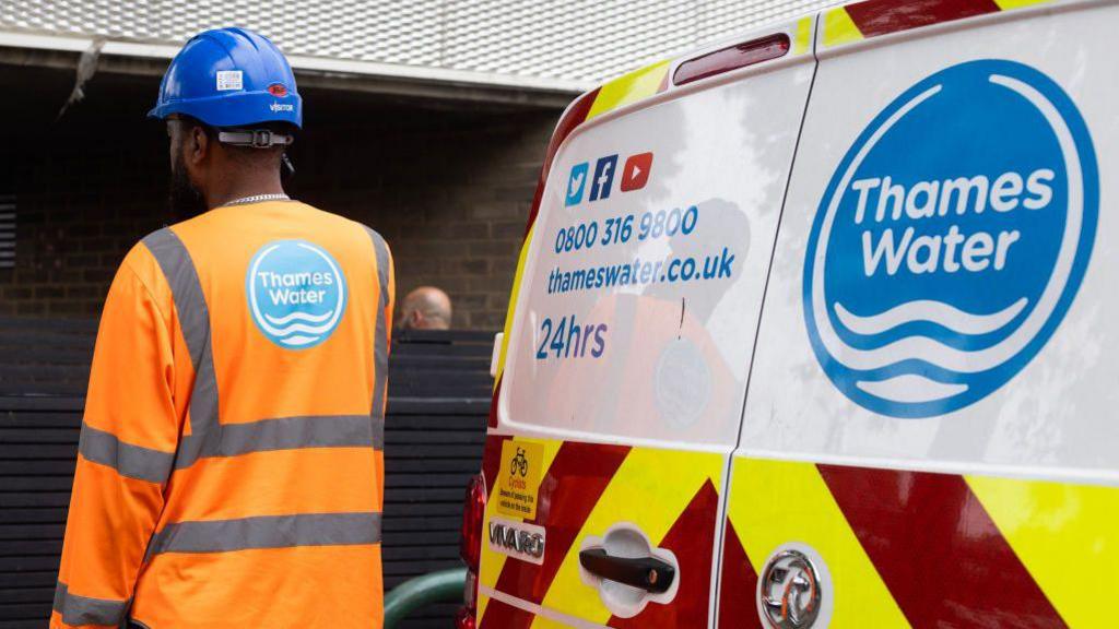 A man wearing a blue hardhat and an orange hi-viz jacket with a Thames Water logo next to a Thames Water van