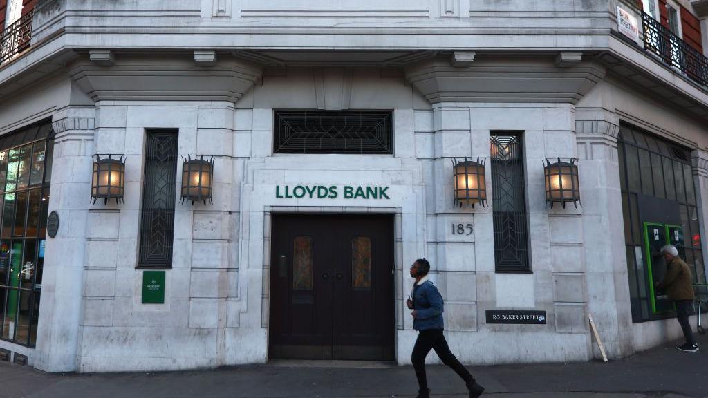 Current image of bank in colour as a man wearing a short coat walks past