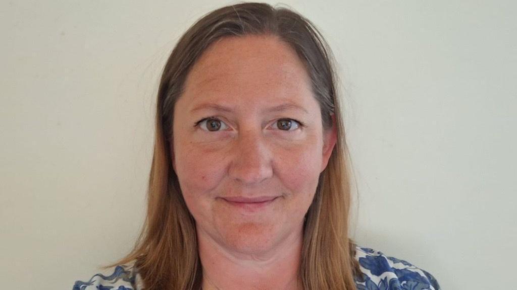 Rachel Bowley is in the middle of the image. She has light brown hair, brown eyes, and is wearing a blue and white patterned shirt.