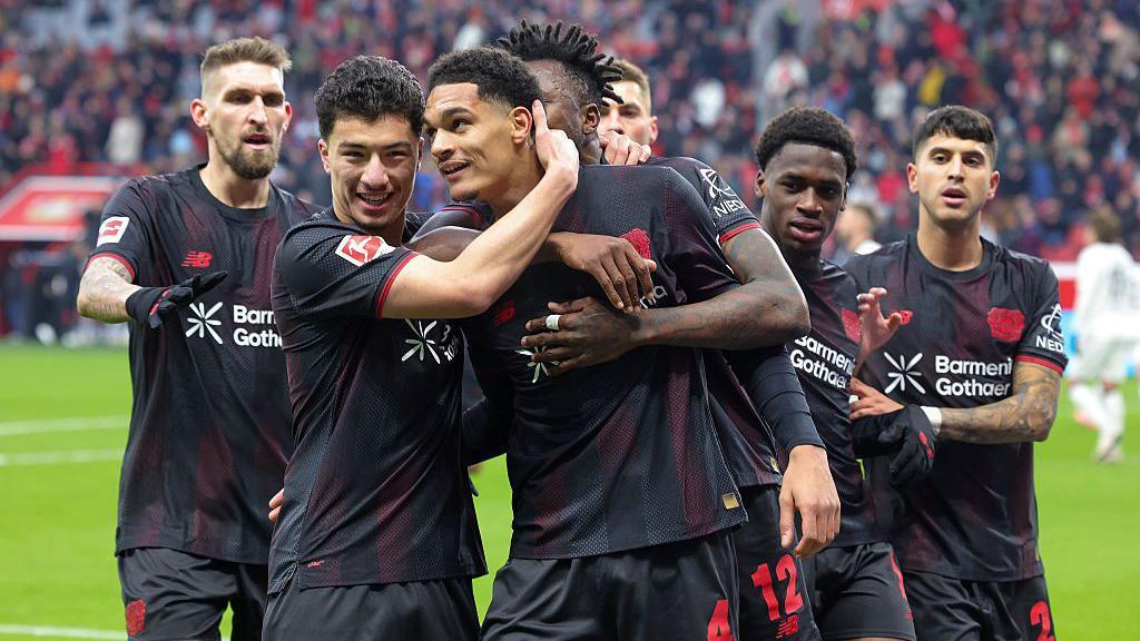 Bayer Leverkusen players celebrate a goal against St. Pauli. They are wearing an all black kit with red trim.