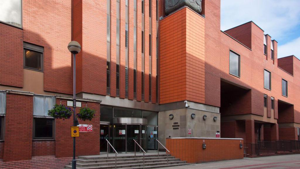 A photo of the entrance to Leeds Crown Court, a multi-storey, red-bricked building.