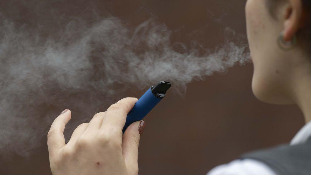 A blue disposable vape being held by a person facing away from the camera