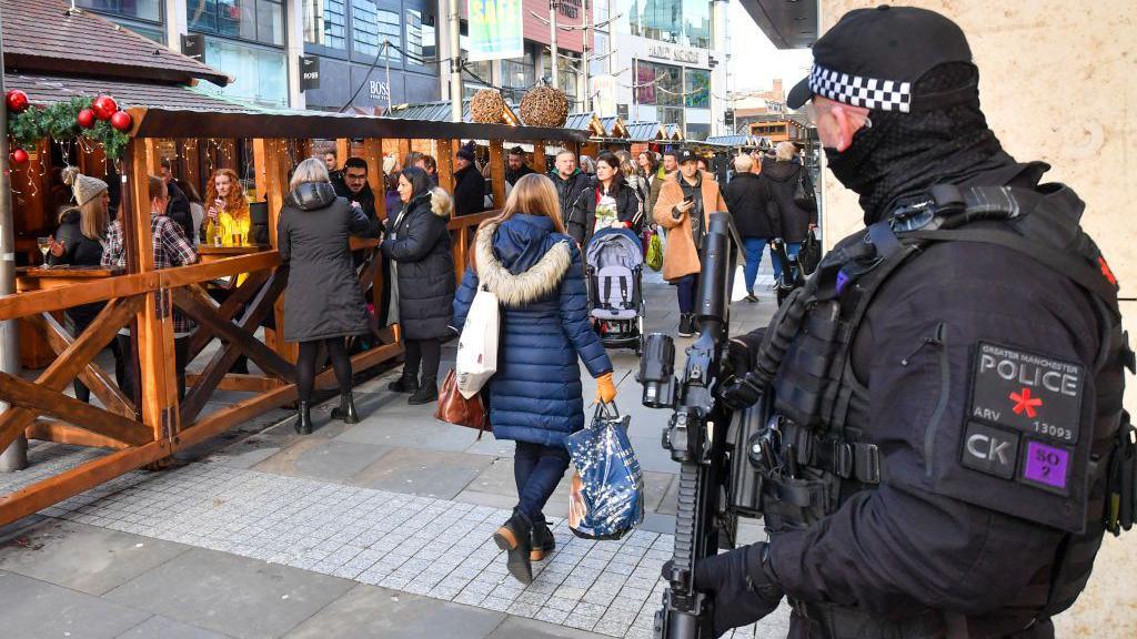 An armed police officer looks at shoppers at a Christmas market