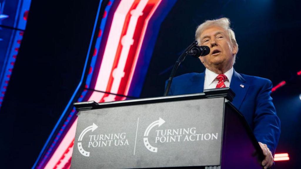 Donald trump in front of a podium with the Turning Point USA logo on it