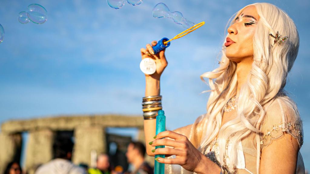 A woman blows bubbles stood in front of Stonehenge