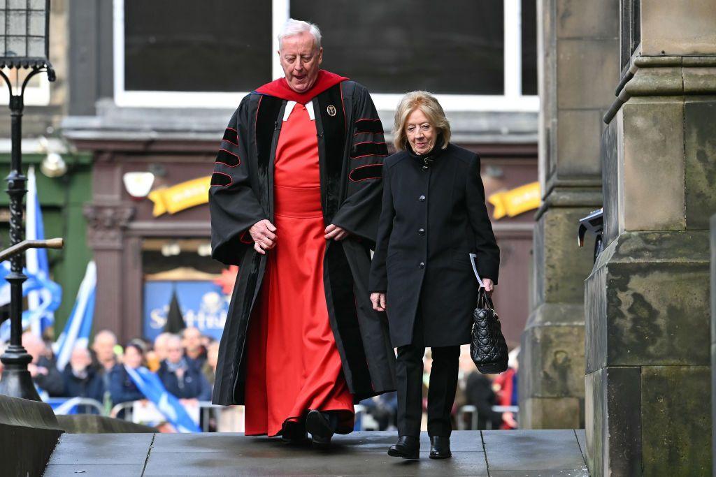 Moira Salmond, with ginger hair and dressed in black, walks into the service with Rev Dr George Whyte, with grey hair and a red and black gown. 