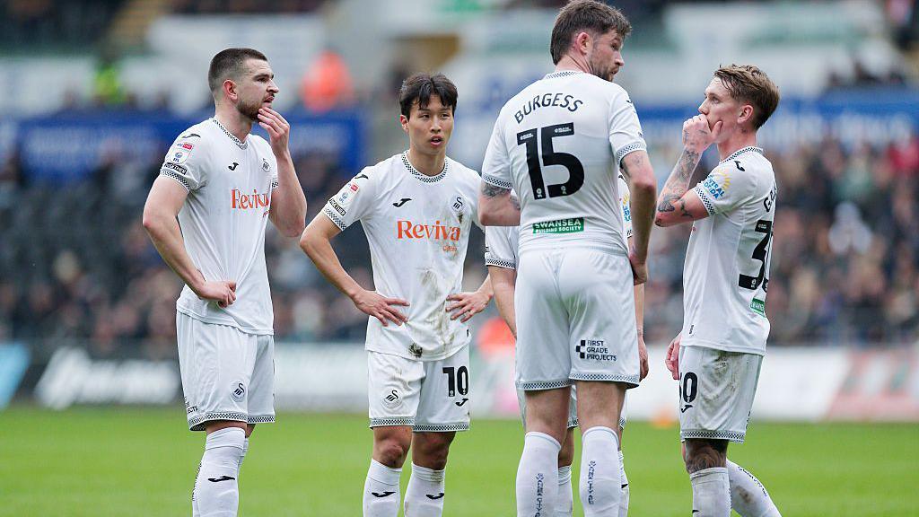 Swansea players rub their chins while standing over a free-kick