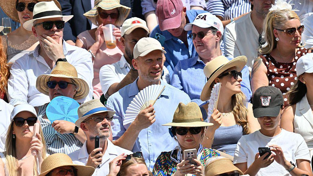 Spectators seen wearing sunhat and using fans in the crowd
