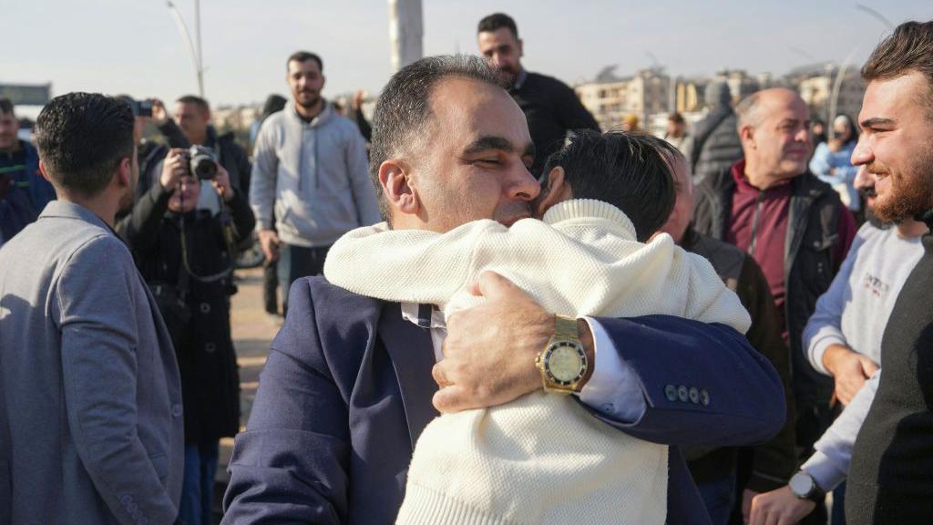 A man embraces a child at the entrance of Aleppo city, on December 9, 2024, as people wait for the return of relatives after the release of detainees from Syrian government prisons following the ousting of Syria's president.