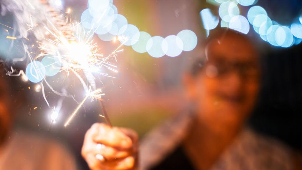 An out-of-focus woman holds a sparkler