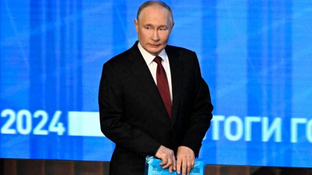 Putin walks on stage holding a folder