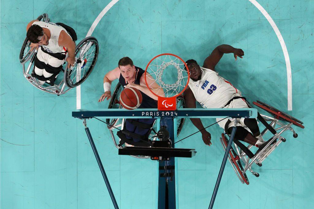 photographed from above the basketball net on the wheelchair basketball court with the players looking on as Lee attempts to make a basket