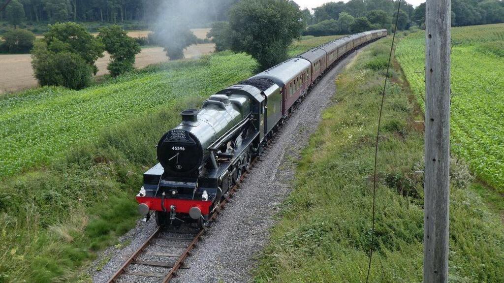 An old steam train painted black and red on a railway line travelling through the countryside in Somerset