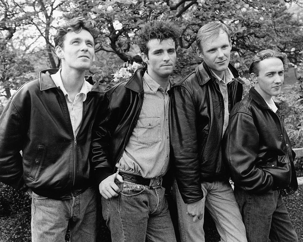 A black and white publicity shot of young Wet Wet Wet members Graeme Duffin, Graeme Clark, Marti Pellow and Tommy Cunningham, all in jeans and leather jackets, posing outside with trees in the background