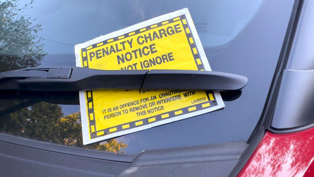 Yellow penalty charge notice placed under a car window wiper