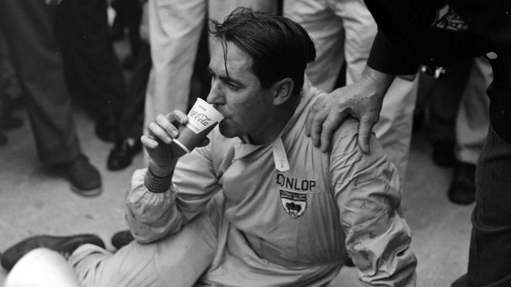 An exhausted Jack Brabham takes a drink after pushing his Brabham over the line to win the 1959 title