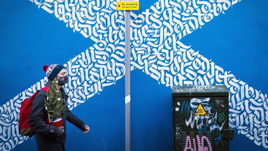 Man in mask walking past a saltire sign