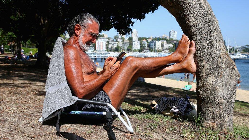 A beachgoer reads his phone in the sun in Sydney on Tuesday