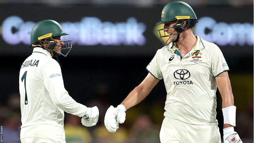 Usman Khawaja and Pat Cummins touching gloves at the end of an over