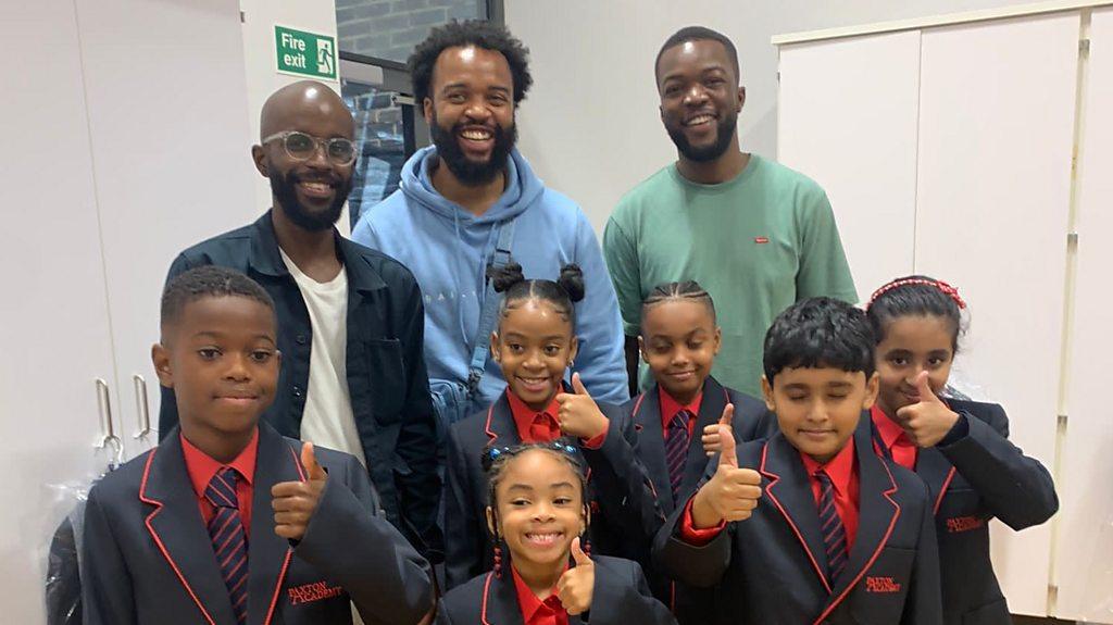 Rapper Jords and school children in uniform giving thumbs up sign.