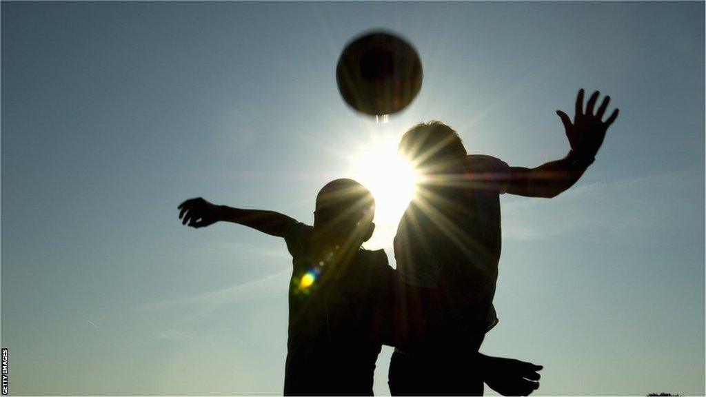 Two silhouetted footballers heading the ball