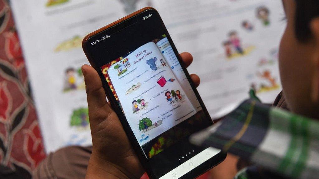 Boy in India with mobile phone and school textbook.