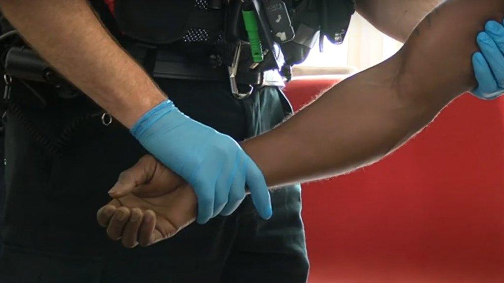 Close-up of suspect's arm being held by a police officer wearing blue latex gloves