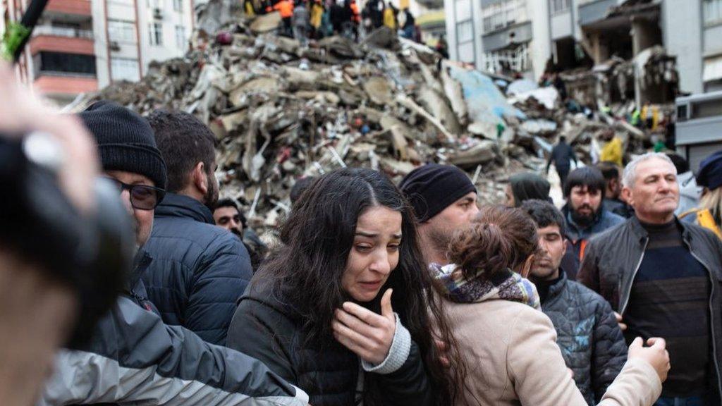 A woman in tears with a mound of rubble behind her.