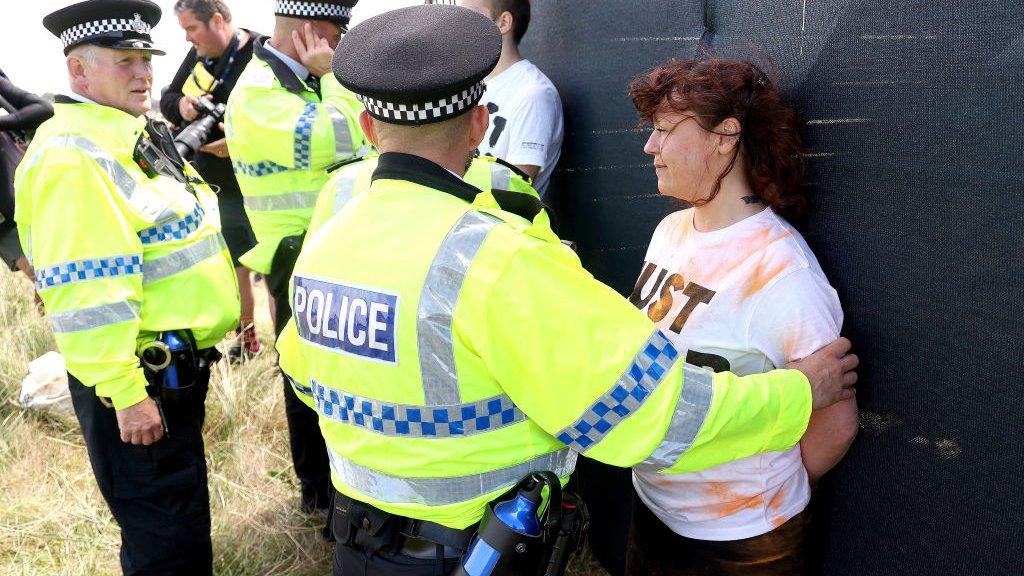 Police detain a protester at The Open