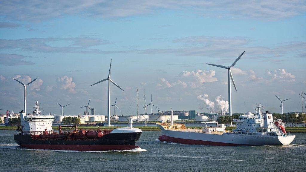 Cargo ships on a canal with wind turbines in the background