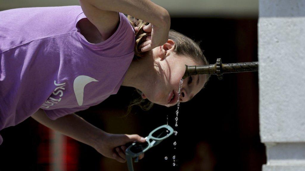 A woman drinks water from a fountain during hot weather in Bosnia