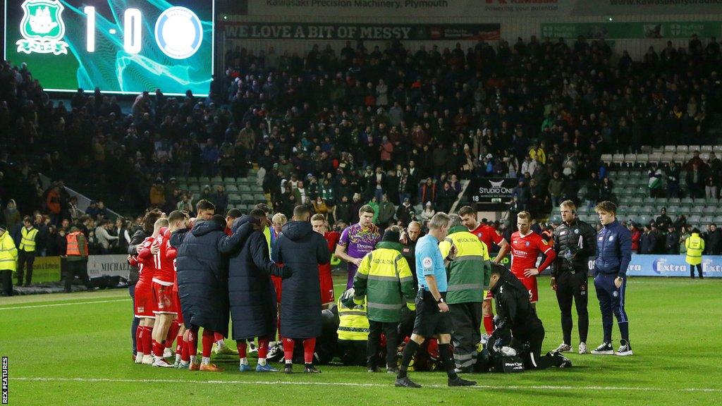 Wycombe players form a barrier around team-mate Tjay De Barr