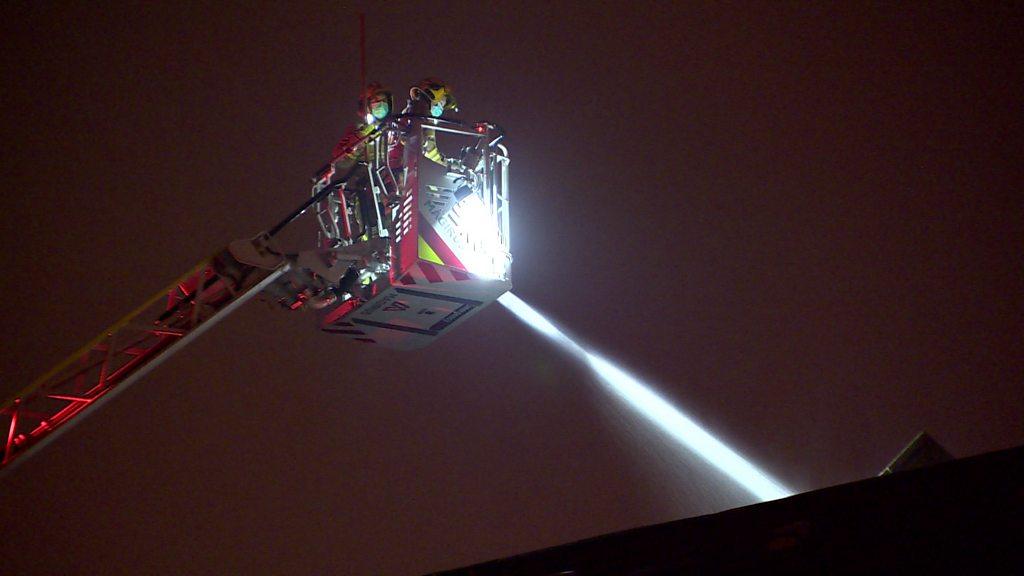 Firefighters on a hydraulic lifting appliance attempt to deal with the fire on the roof of the building