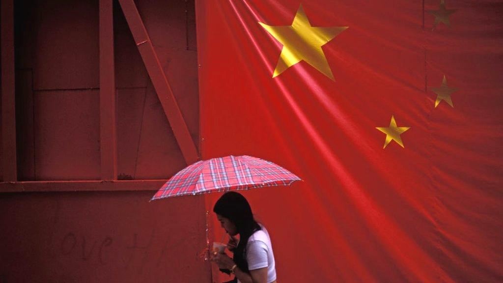 A woman with an umbrella walking under the Chinese flag