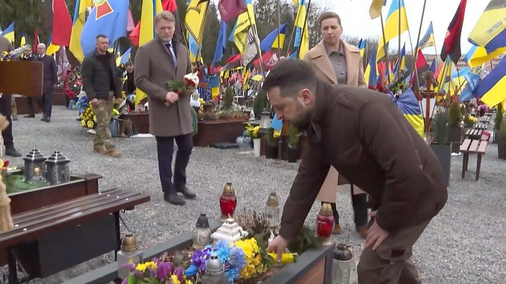 President Zelensky laying flowers, surrounded by Ukrainian flags