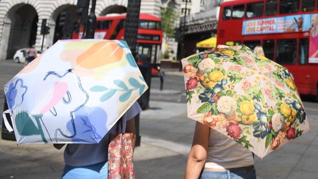 People using umbrellas to shelter from the sun in London in summer 2022