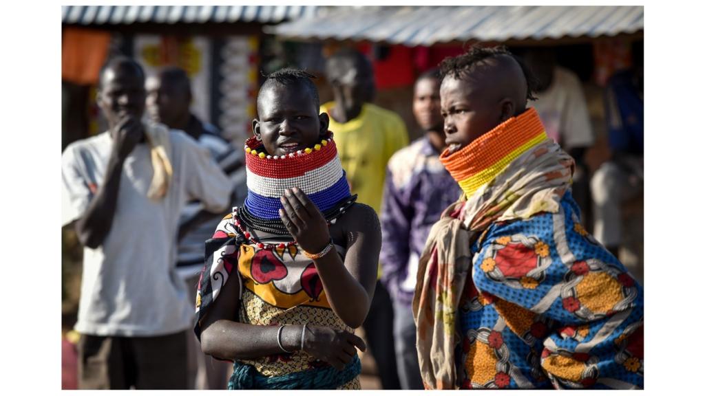 Women in elaborate neck adornements from the local Turkana community look on at Kalobeyei refugee settlement scheme in Kakuma