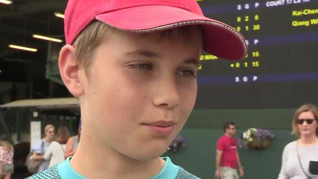 Boy in hat outside Wimbledon score board