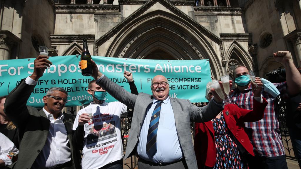 Former post office worker Tom Hedges (centre) holds up a bottle and glass of champagne in celebration outside the Royal Courts of Justice, London