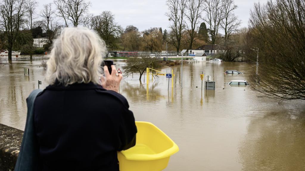 A person takes a picture with submerged cars in the background, following flooding in Wallingford on 5 January