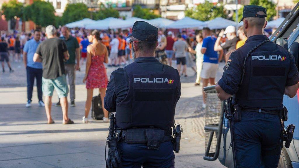 Two policemen watch fans gathered in Seville