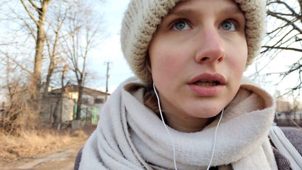 Woman walking down a country lane speaking into headphones