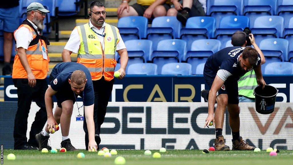 Reading FC staff with buckers collect tennis balls from the field at the Select Car Leasing Stadium.