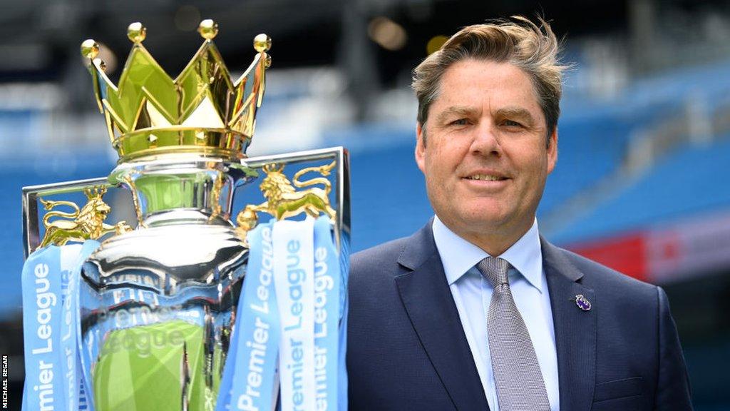 Richard Masters smiles next to the Premier League trophy