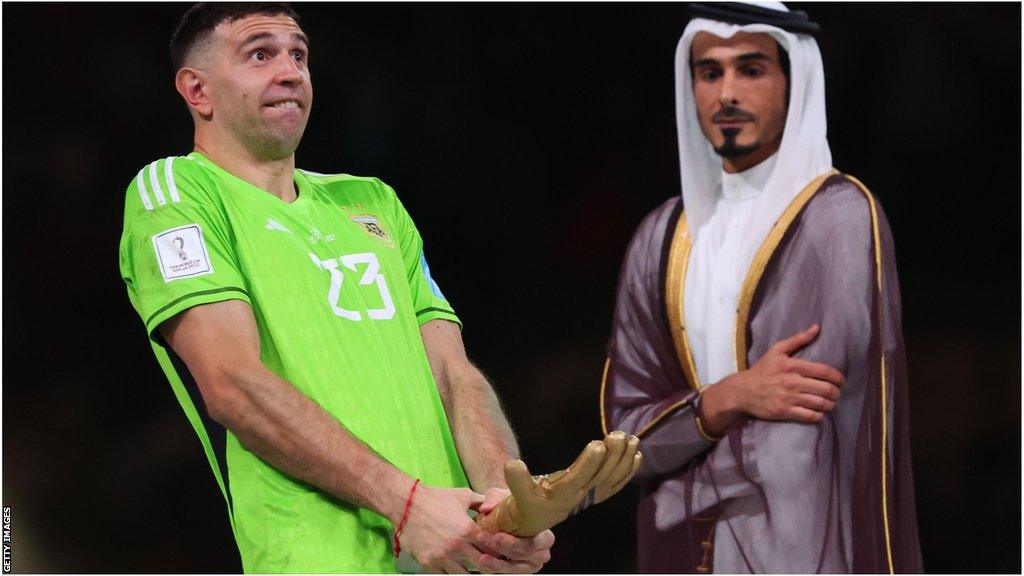 Martinez celebrates with World Cup Golden Glove trophy in Qatar, whilst Qatari politician watches on.