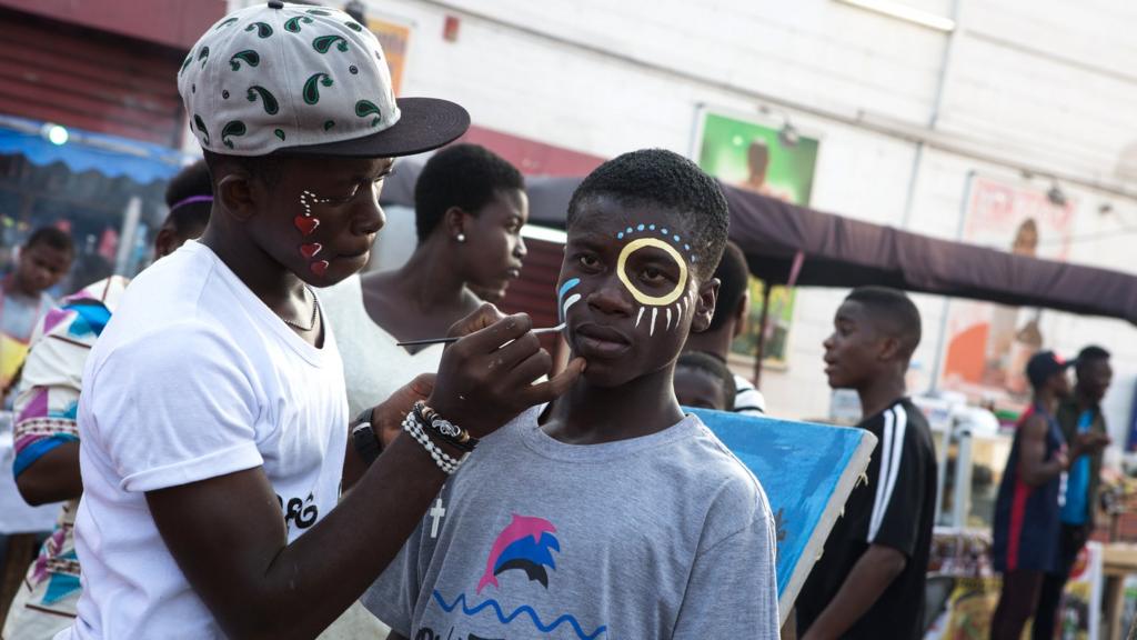 A picture taken on August 19, 2017 shows a man painting the face of a boy during the annual Chale Wote Street Art Festival at James town in Accra